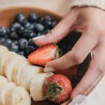 A wooden bowl filled with fresh bananas and berries held by an unrecognizable person's hands.