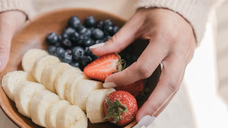 A wooden bowl filled with fresh bananas and berries held by an unrecognizable person's hands.